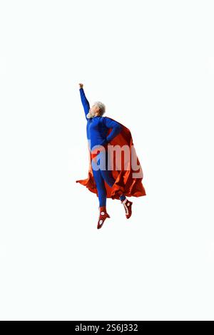 A man in blue superhero costume and red cape flying upward with fist raised, showcasing energy, determination, and personal achievement Stock Photo