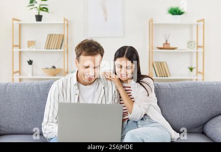 Young couple at laptop computer screen watching, planning budget, reading late news email, smiling  Stock Photo