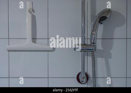 Paris, France - 01 12 2025: A squeegee and a shower head hanging on tiled wall Stock Photo