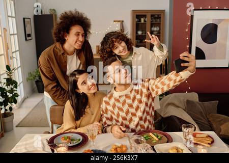 High angle shot of biracial company of friends sitting at festive table and taking selfie together Stock Photo
