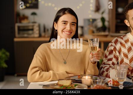 Smiling young adult brunette smiling widely and raising her glass with champagne while posing for portrait Stock Photo