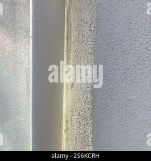 A detailed view of a building corner showcasing two contrasting wall textures, one smooth and the other rough, illuminated by natural daylight. Stock Photo