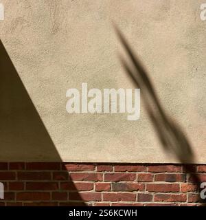 Shadow cast on a beige wall above a brick facade, showcasing minimalistic architectural textures and natural light interplay Stock Photo