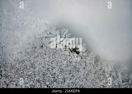A detailed close-up of frost patterns on a glass window, showcasing intricate ice crystals with a gradient from dense frost to a smoother, clear surfa Stock Photo