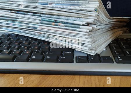 A stack of newspapers is on the computer keyboard Stock Photo