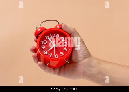 Red alarm clock in hand on beige background. Time concept Stock Photo