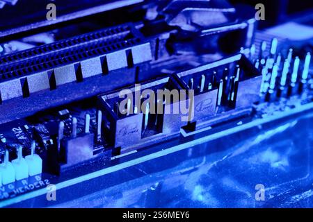 A detailed close-up of various motherboard connectors and pins illuminated by blue lighting. The high-contrast image highlights the structure and conn Stock Photo