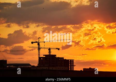 A city skyline at dusk with a gradient sky transitioning from warm orange to deep blue. The silhouettes of buildings and cranes are visible against th Stock Photo