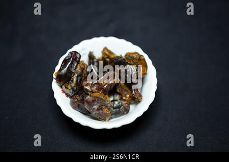 fresh dates in ceramic bowl studio shot of on black background Stock Photo