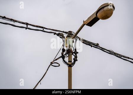 A street light is lit up in the middle of a cloudy day. The light is surrounded by wires and is the only source of light in the area Stock Photo