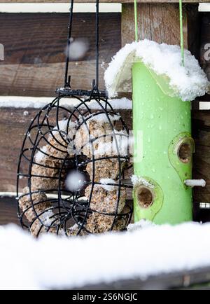 A bird feeder with a green tube and a black one with a wreath on it. The wreath is covered in snow Stock Photo