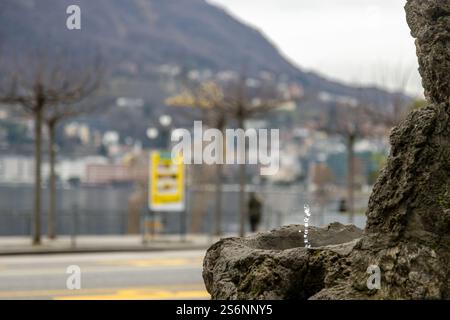 Drinking water fountain in the center of Lugano, with the lake and mountains in the background, Switzerland Stock Photo