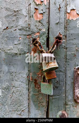 A green door with a chain and three locks hanging from it. The door is old and has a rustic appearance Stock Photo