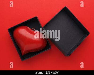 Red metal heart in a black gift box on red background, Valentines or Birthday concept Stock Photo