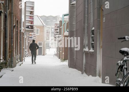 A man, seen from behind, walks along a snow-covered, narrow Dutch street. Creating a tranquil and picturesque scene in a charming snowy Netherlands to Stock Photo