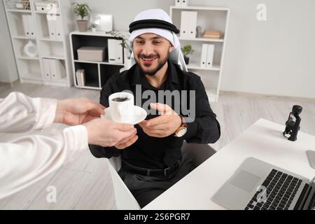 Arab businessman taking coffee from secretary at table in office Stock Photo