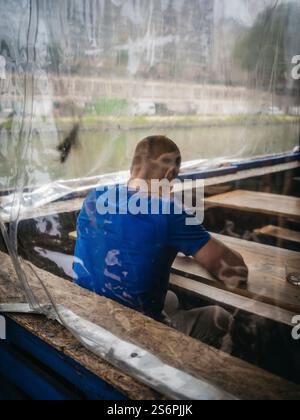 Back view of a man by the river behind a tarpaulin Stock Photo