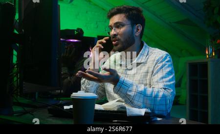 Stressed Arabian Indian man male guy looking code coder programmer technology talk mobile phone error hacker problem loss worker computer trouble IT Stock Photo