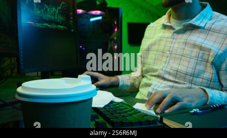 Pensive Caucasian man professional software engineer guy male coder programmer crypto specialist drinking coffee workplace looking computer thinking Stock Photo