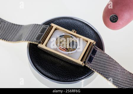 Watch case open, watch battery lying on fingertip, detail, white background, symbol photo, battery change, watch repair, Stock Photo