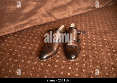 Classic brown leather dress shoes featuring black tips and buckles elegantly positioned on patterned carpet flooring fashion concept Stock Photo