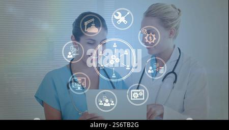Image of business icons over caucasian female doctors talking Stock Photo