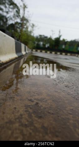 Close-up of a wet road with a puddle reflecting the sky, bordered by a black and white curb. Stock Photo