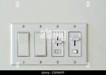 A fixture of mixed rocker switches and light dimmers installed on a white wall Stock Photo
