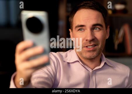 Close-up Man businessman holding phone in hand looking into screen video call and selfie and smile with teeth. A handsome young guy is chatting on a v Stock Photo