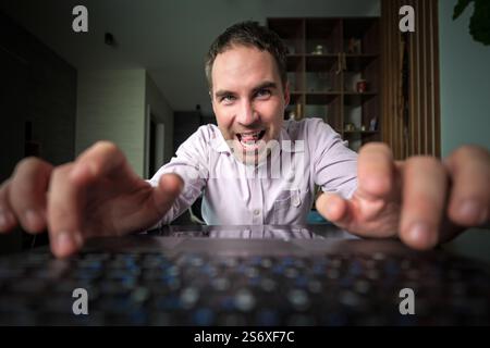 A young handsome man in a pink shirt is working at a computer on a light background. the nerd looks at the monitor screen picking his teeth with his f Stock Photo