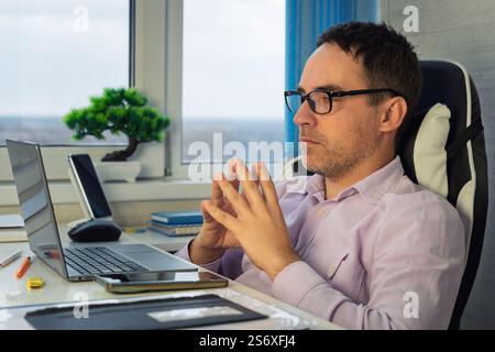 He is using touchpad while reading an e-mail on laptop. Multi-tasking businessman working in the office. man works in a bright office during the day Stock Photo