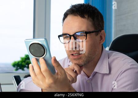 Portrait of cheerful brunette man in shirt using cellphone , reading good news message, enjoying mobile application. Stock Photo