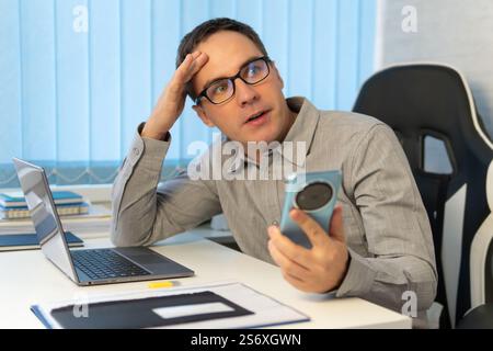 thoughtful businessman in a blue shirt holding a phone and looking thoughtfully at the screen. A young man is carefully reading messages on a smartpho Stock Photo