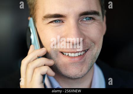 Young successful businessman boss talking on phone close up, man smiling contentedly inside office at workplace in business suit. Hilarious phone conv Stock Photo