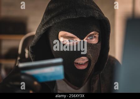 a male thief holds a credit card in his hand and picks up a password to steal money. theft from electronic wallets Stock Photo