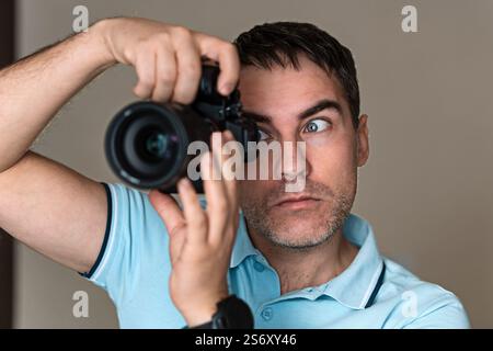 Surprised young man tourist holding photo camera. blue background. reporter makes an amazing shot. Photographer surprised by the picture. The paparazz Stock Photo