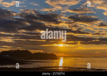 Sun appearing from behind the clouds sending a streak of sunlight across the sea and mud Stock Photo