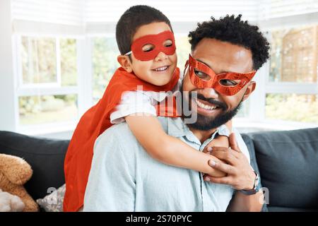 Father, child and superhero costume in home, hug son and playing fantasy games together on couch. Dad, boy and embrace kid for halloween cosplay in Stock Photo
