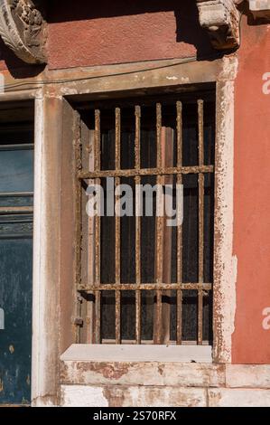 Rusty barred window on a weathered Venetian building.  A glimpse into a historical facade. Stock Photo