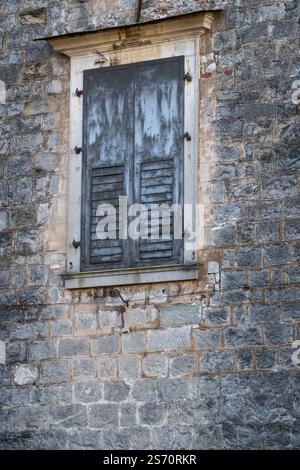 Close-up of a weathered stone wall with a gray shuttered window.  Aged stonework and weathered shutters. Stock Photo