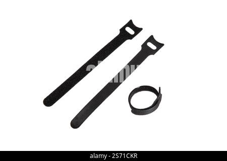 Three black hook-and-loop cable ties, two flat and one coiled, used for organizing and securing cables, wires, or items, isolated on a white backgroun Stock Photo