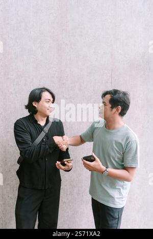 Two men shake hands after reaching an agreement related to the content on a mobile phone, symbolizing successful communication and collaboration. Stock Photo