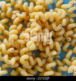 A detailed close-up image of uncooked spiral pasta showcasing their intricate texture and bright yellow color, placed on a light vibrant background. Stock Photo