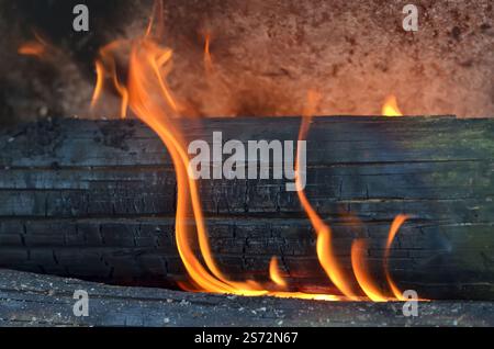 Black charred logs engulfed in flames in a fireplace. Stock Photo