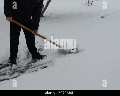 man in black clothes shoveling fresh snow from lawn, path or front yard, clearing snow cover after snowfall with hand shovel, domestic winter routine Stock Photo