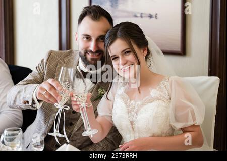 A newly married couple joyfully raises their champagne flutes in a toast. The bride wears a beautiful white dress, and the groom is in a brown suit. P Stock Photo