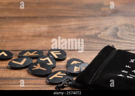 A wooden rune set for divination, magic, and spiritual practices, displayed with a black velvet pouch and empty space on a wooden table. Stock Photo