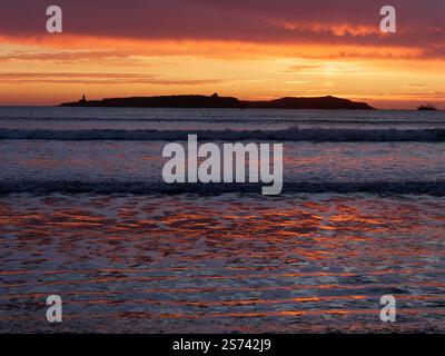 Dramatic dark clouds at sunset over an Island off the coast of Essaouira as the fiery sky is reflected in the water, Morocco. Jan 18, 2025 Stock Photo