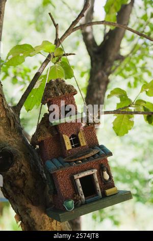 Close-up of wooden and granulated exterior finished birdhouse hanging from Malus domestica - Apple tree branch in backyard garden in summer. Stock Photo