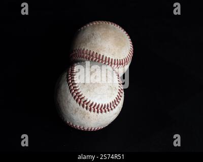 A minimalist composition featuring two baseballs viewed from above, isolated on a sleek black background, highlighting their texture and simplicity. Stock Photo